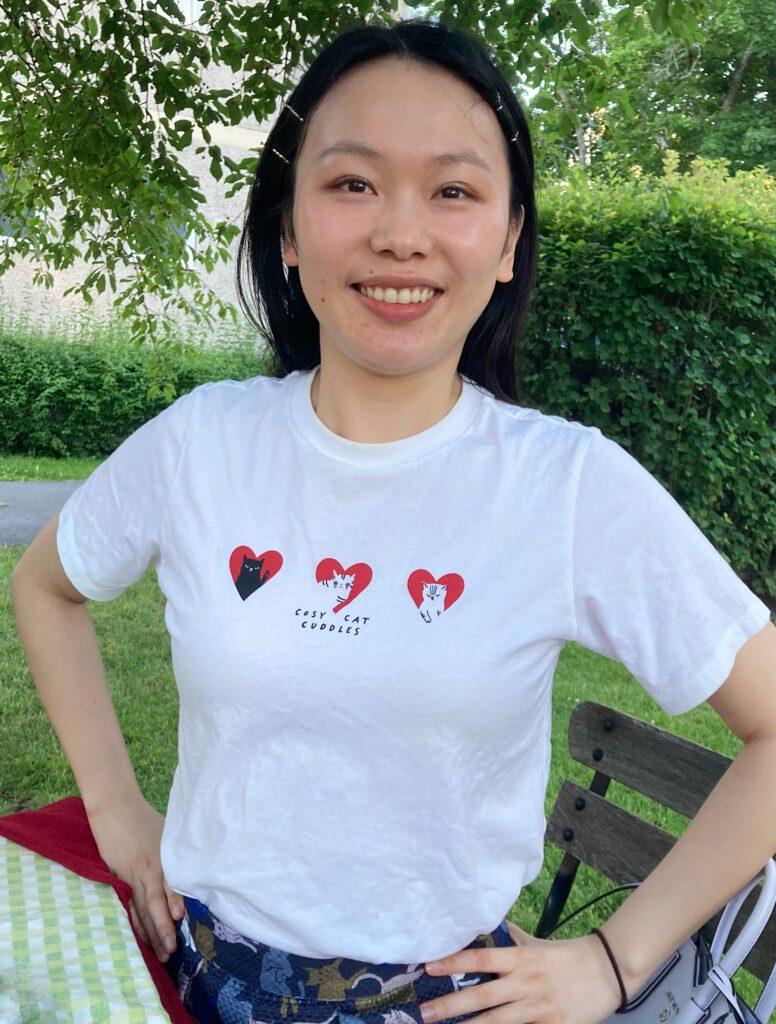 Young woman wearing white Uniqlo UT “Cosy Cat Cuddles” T-shirt featuring Marie Åhfeldt’s cat illustrations.